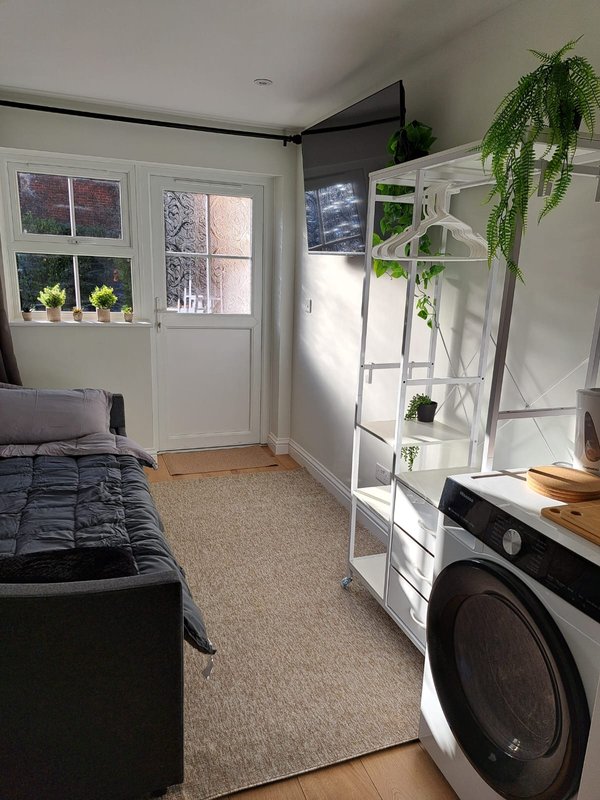 Bright bedroom with single bed, washing machine, shelving unit with plants and natural light from doors
