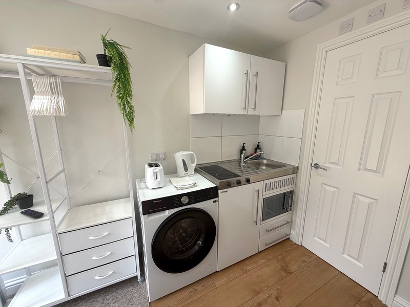 Compact kitchenette with white cabinetry, integrated appliances, and shower enclosure visible