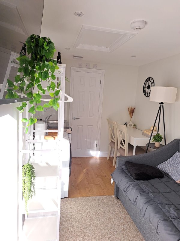 Modern bedroom with bed, desk, hanging plant, wooden flooring and white cabinetry