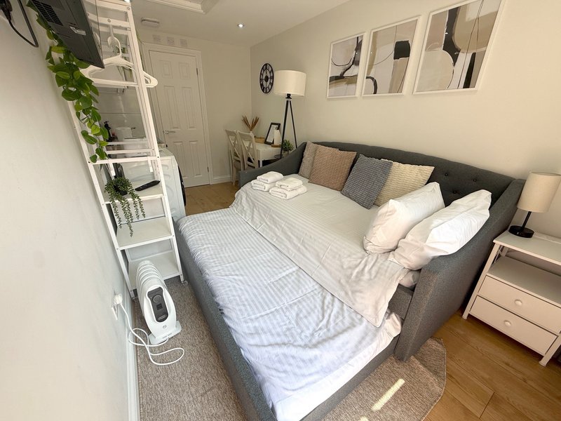 Modern bedroom with double bed, grey headboard, white bedding, wooden floor and wall shelving