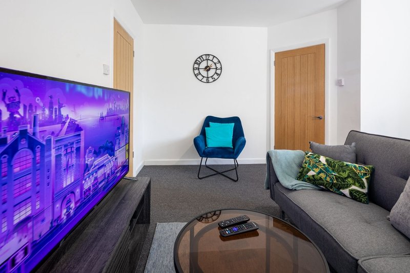 Modern living room with grey sofa, TV, turquoise chair, wooden doors and wall clock