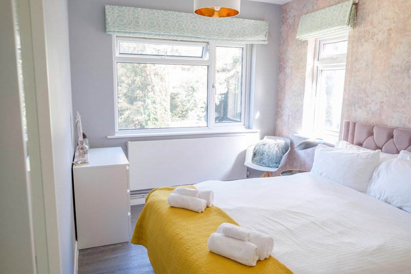 Bright bedroom with double bed, yellow throw, white pillows and windows overlooking garden