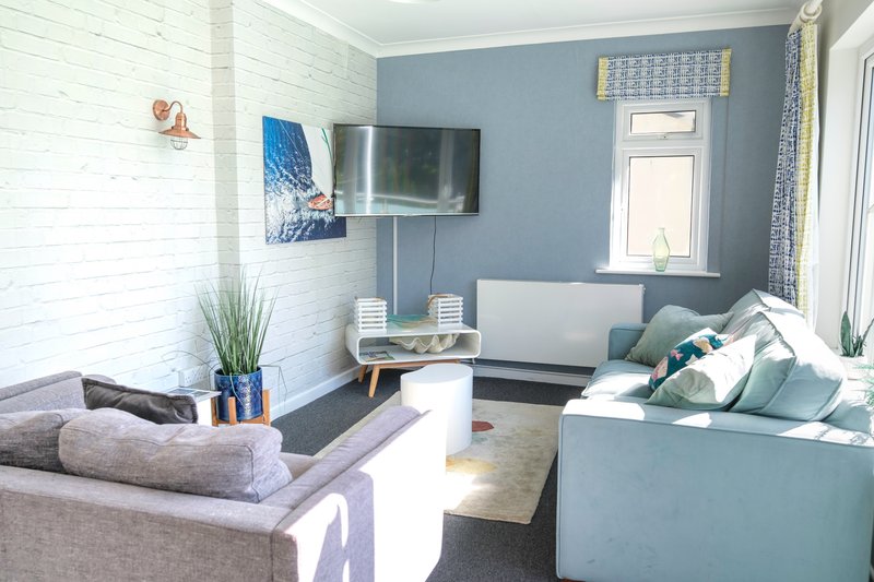 Modern living room with blue walls, grey sofa, wall-mounted TV and natural light from windows