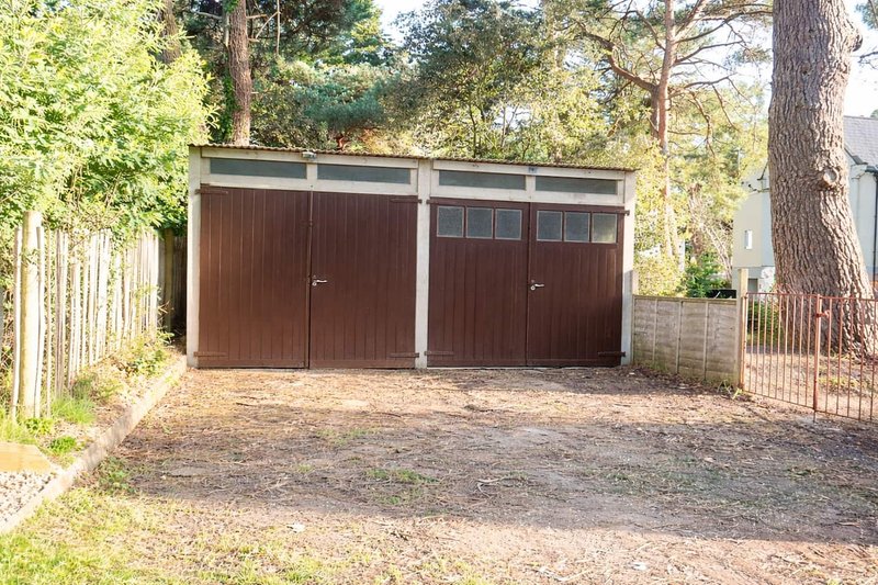 Double garage with brown doors, gravel driveway, surrounded by trees and fencing