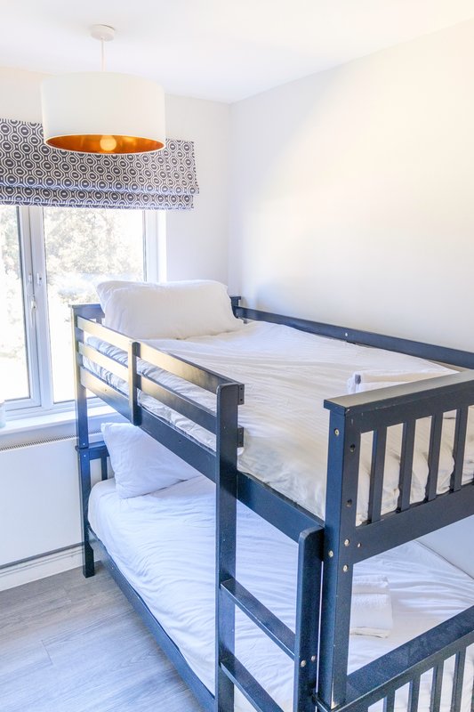 Bright children's bedroom with bunk beds, navy blue frames, pendant lamp, and window with patterned blind.