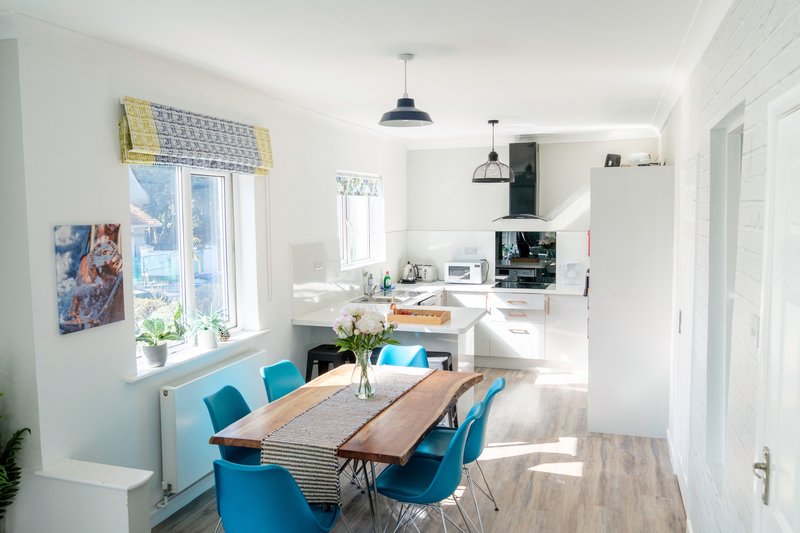 Bright open-plan kitchen and dining area with blue chairs, wooden table, and modern pendant lighting