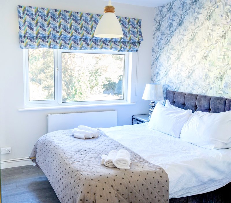 Bright bedroom with double bed, patterned headboard, window with blue valance, pendant lamp
