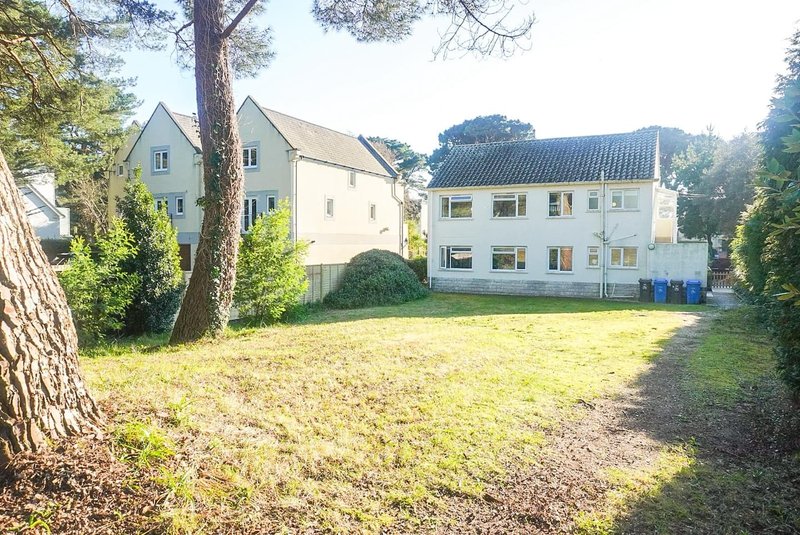Residential properties viewed from a grassy garden area with large tree and hedges