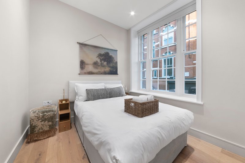 Bright bedroom with double bed, white bedding, wooden floor and large window overlooking street