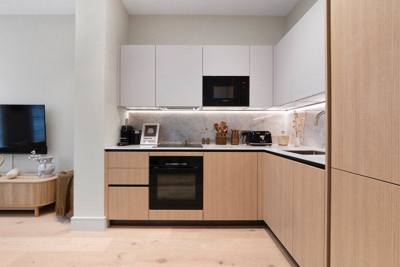 Modern kitchen with light wood cabinetry, white upper cabinets, marble backsplash and black appliances