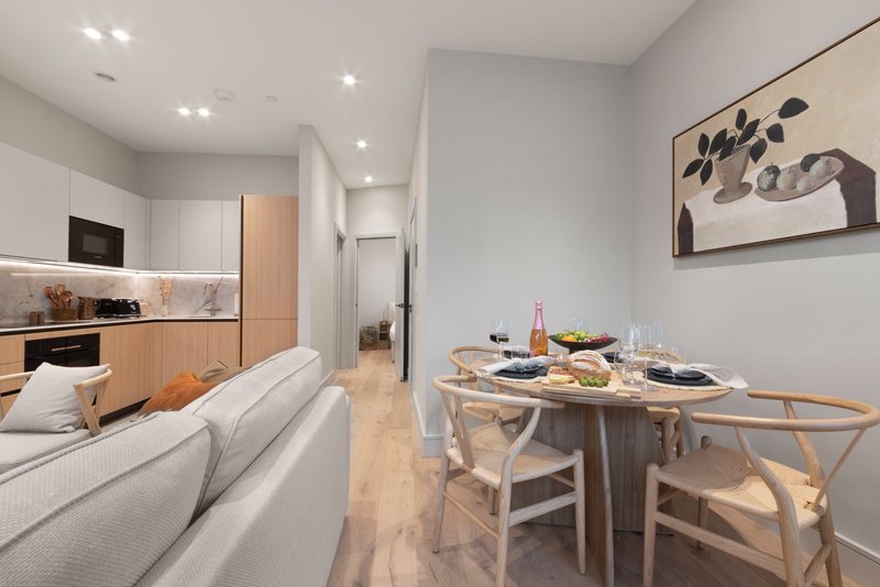 Open-plan kitchen and dining area with light wood flooring, white sofa, and dining table set for two
