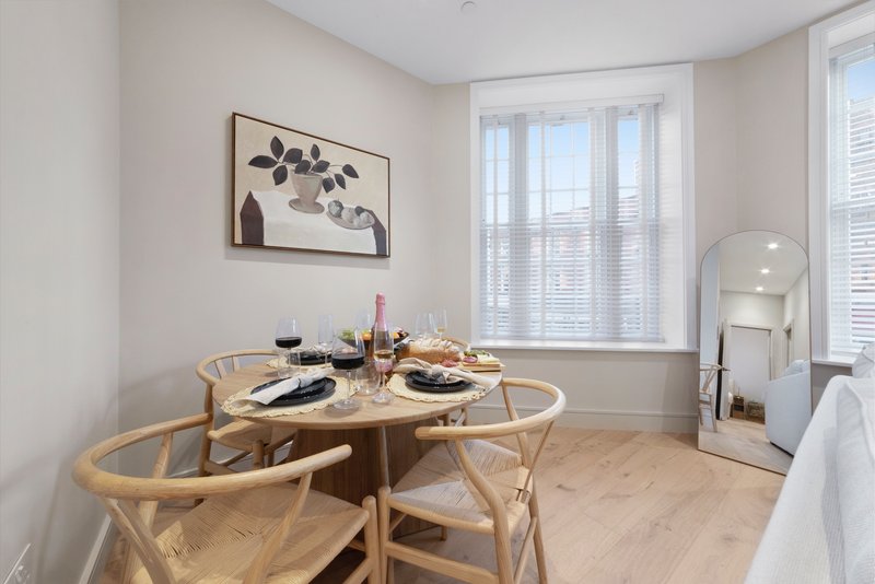 Bright dining area with round wooden table, wishbone chairs, and large windows with shutters