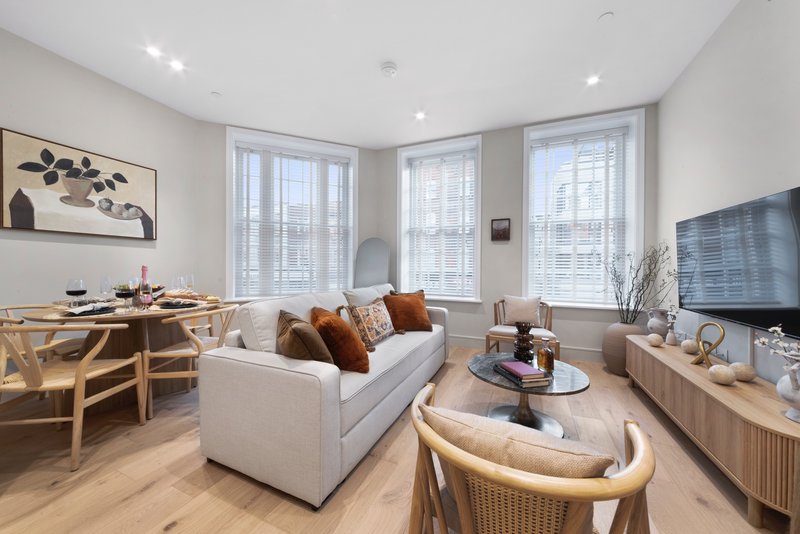 Modern open-plan living room with white sofa, wooden dining table, and large windows