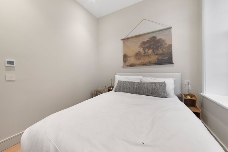 Bright bedroom with single bed, white bedding, gray cushion, and framed landscape artwork