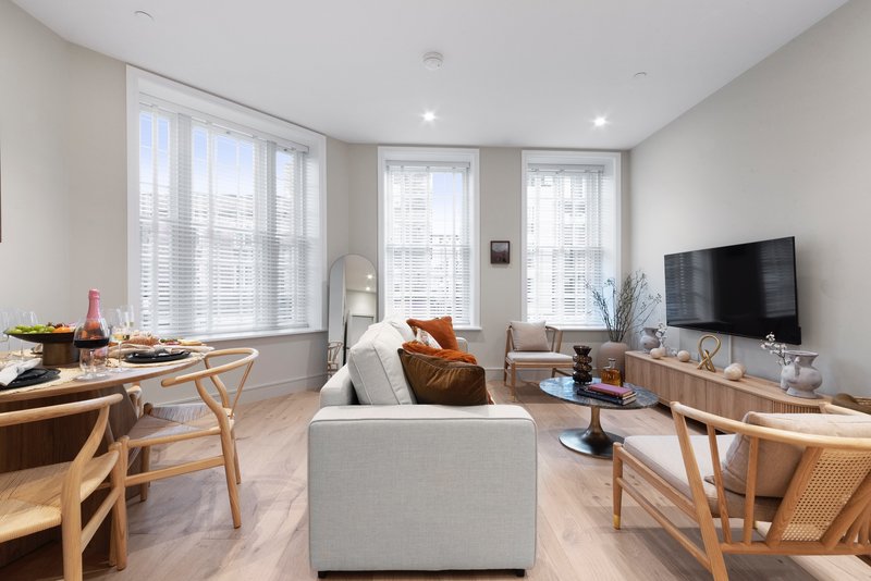 Bright modern living room with cream sofa, wooden furniture, TV, and large windows