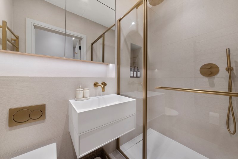 Modern bathroom with white vanity, mirror, walk-in shower and brass fixtures