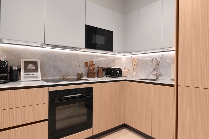Modern kitchen with white and wood cabinetry, black appliances, and marble backsplash