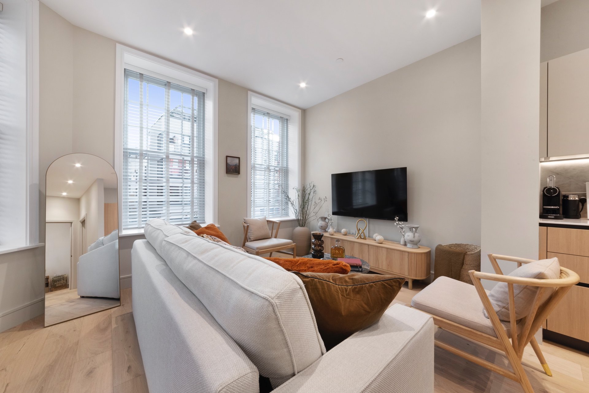 Modern open-plan living room with sofa, TV, dining chairs and kitchen area visible