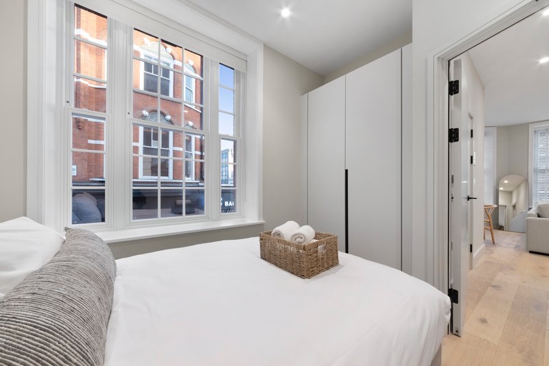 Bright modern bedroom with white bedding, large window overlooking street, wooden flooring