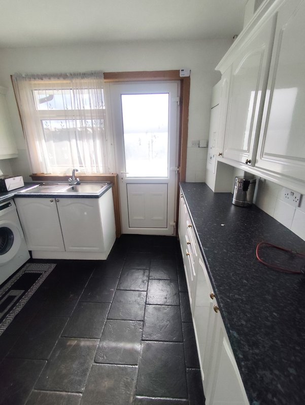 Kitchen with white cabinets, black countertops, washing machine and door to garden