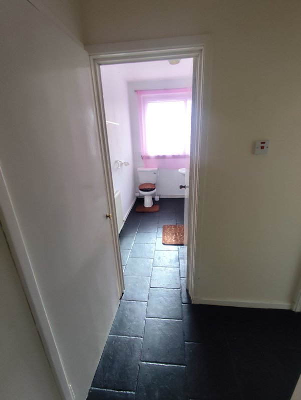 Hallway with dark tile floor leading to bathroom with pink-lit window and white sink