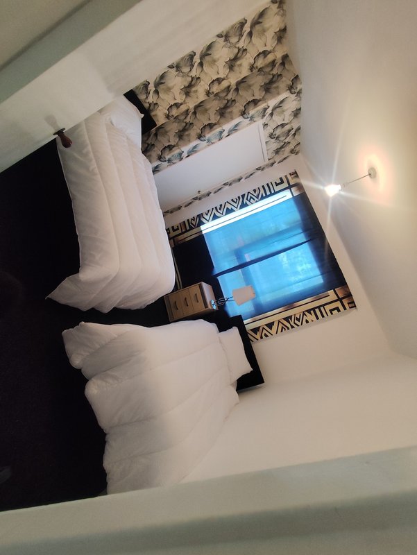 Bedroom with double bed, patterned headboard, window with blue view, and wall sconces