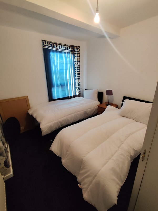 Compact bedroom with two single beds, white bedding, dark headboards and geometric patterned window covering
