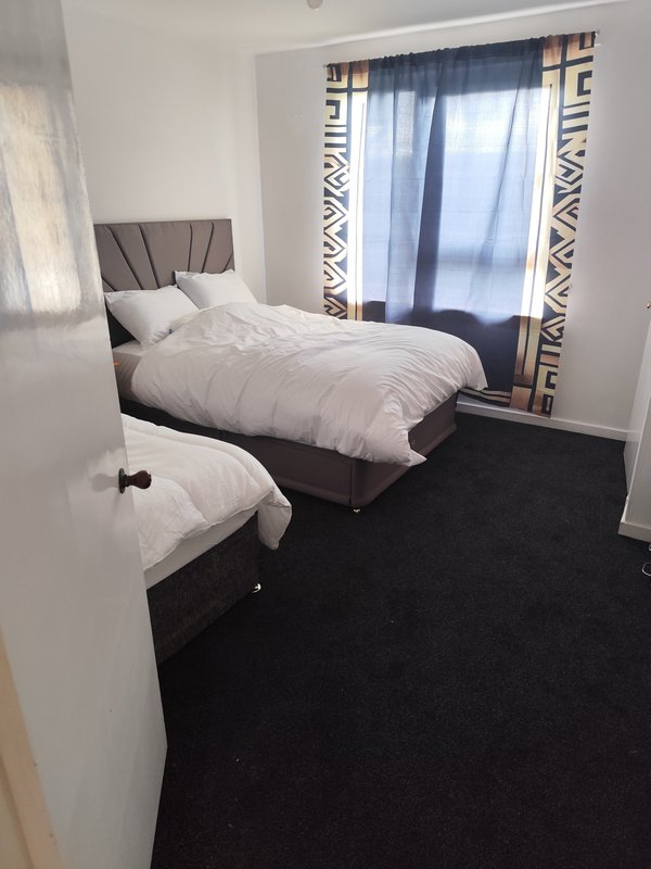Bedroom with double bed, white bedding, dark carpet, and patterned curtains