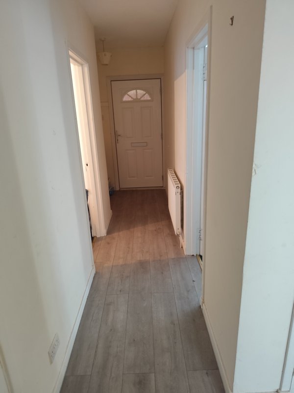 Narrow hallway with light wood flooring, beige walls, and doors leading to other rooms