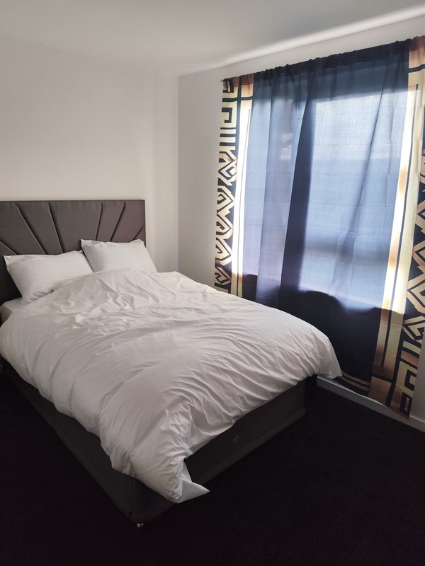 Bedroom with double bed, grey headboard, white bedding, and patterned curtains