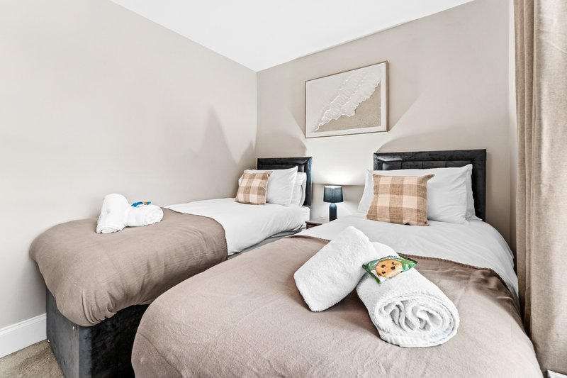 Twin bedroom with two beds, neutral bedding, rolled towels, and wall art