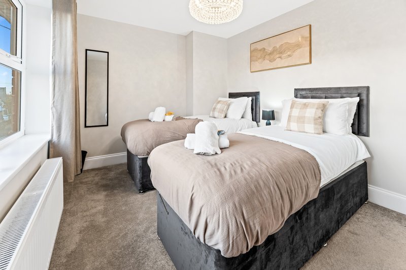 Twin bedroom with two beds, white pillows, beige bedding, and large window