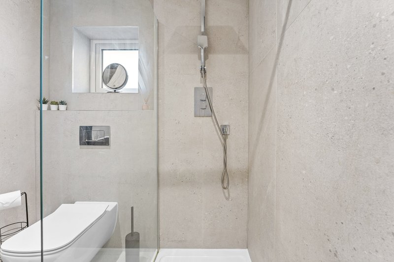 Modern bathroom with walk-in shower, white toilet, small window and beige tile walls