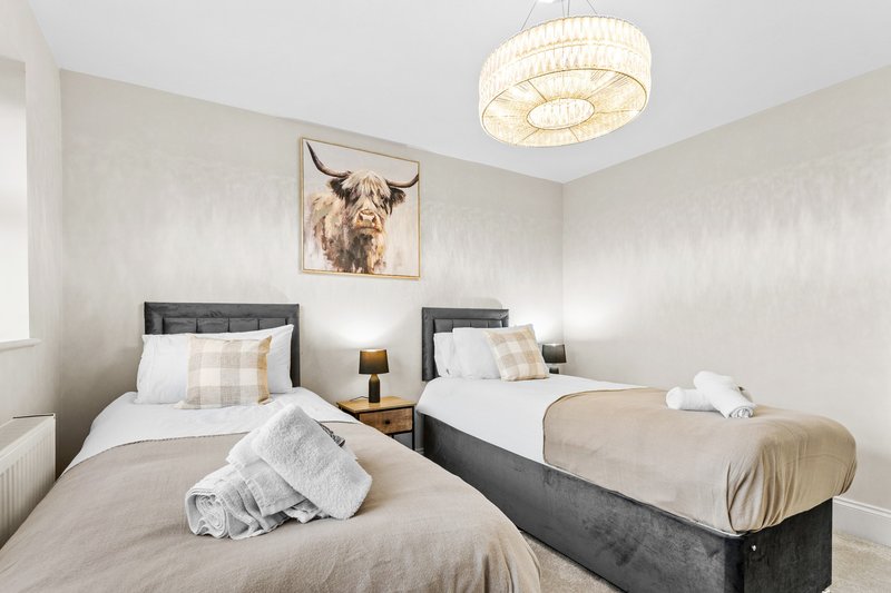 Twin bedroom with two single beds, dark headboards, neutral bedding and framed artwork