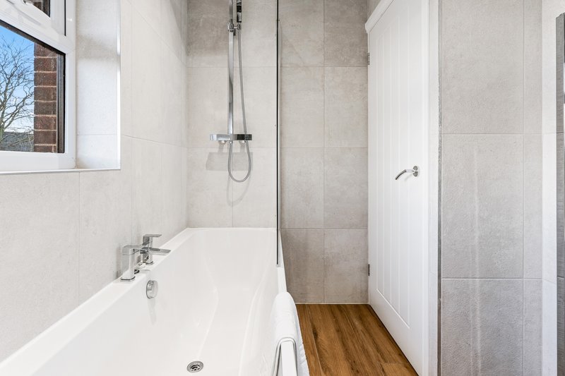Modern bathroom with white bathtub, wooden floor, and walk-in shower enclosure