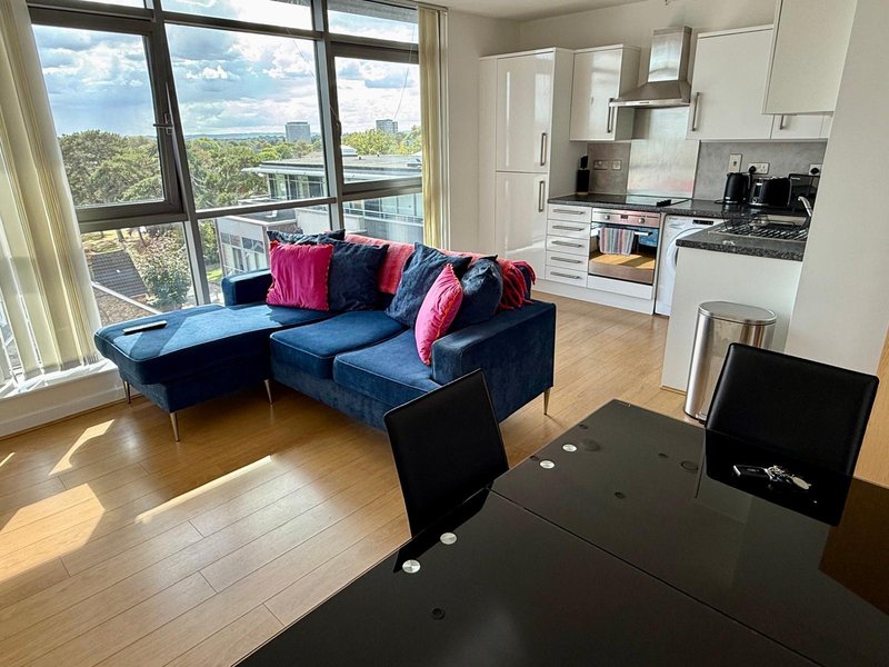 Modern open-plan living area with blue sofa, kitchen, and large windows overlooking river