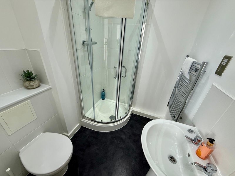 Modern bathroom with corner shower, white toilet, round sink and heated towel rail