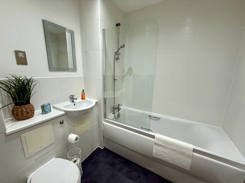 Modern bathroom with white subway tiles, bathtub with glass screen, sink, mirror and toilet