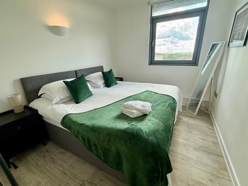 Modern bedroom with double bed, green bedding, grey headboard, and window with countryside view