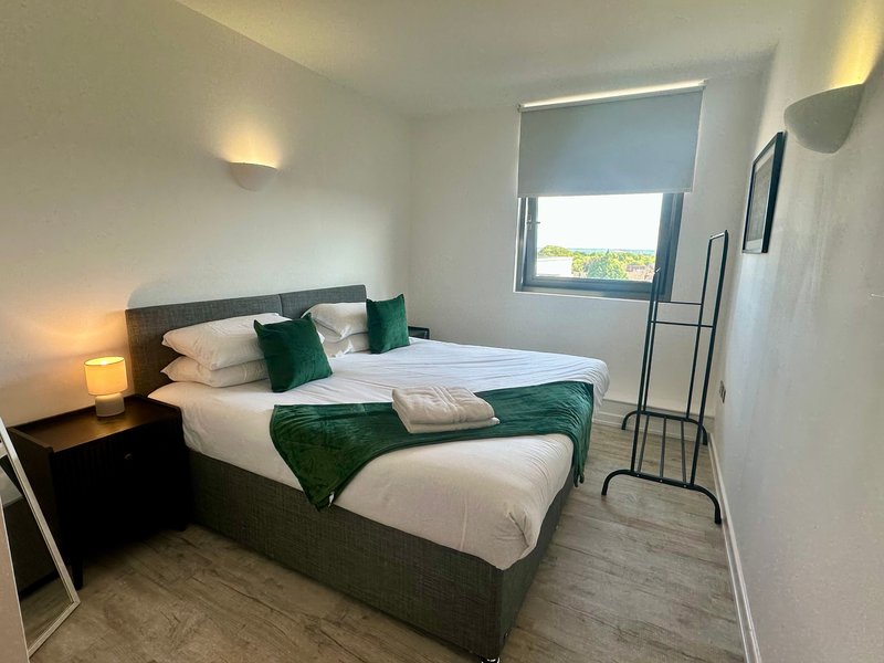 Modern bedroom with double bed, green bedding, bedside lamps and window with blind