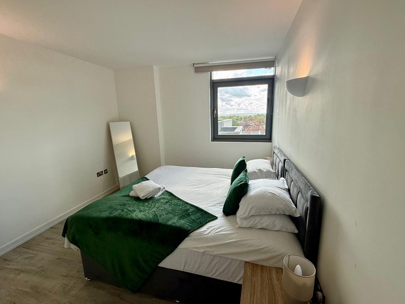 Bright bedroom with two single beds, green bedding, wooden floor and window view