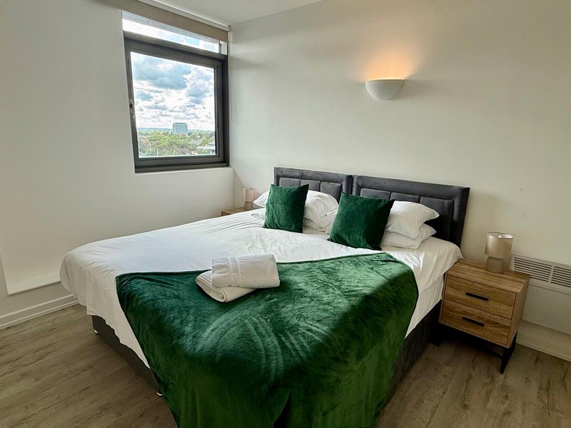 Modern bedroom with double bed, green velvet throw, white pillows and wooden nightstand