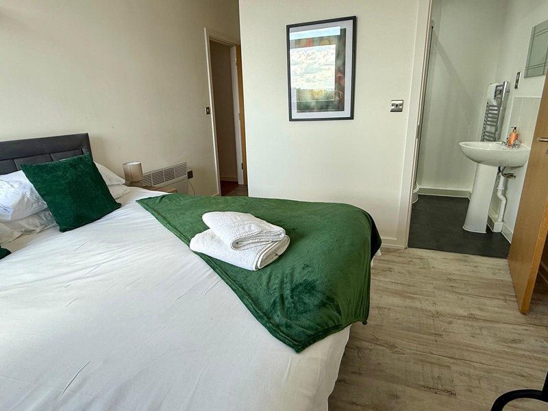 Bedroom with double bed, green bedding, wooden floor, sink and framed wall art