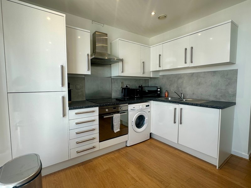 Modern kitchen with white cabinets, black cooktop, washing machine and wooden flooring