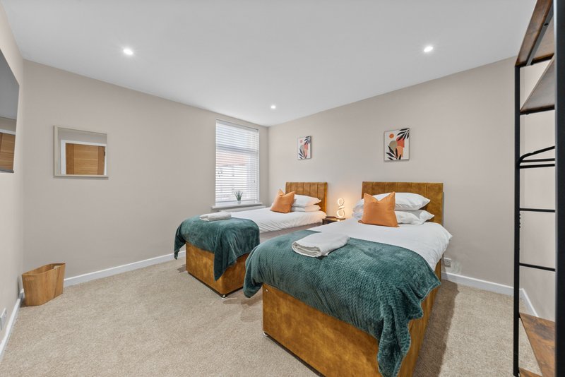 Bright twin bedroom with two wooden beds, green bedding, orange pillows and neutral carpeting