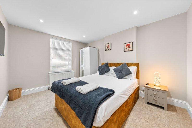 Modern bedroom with wooden bed, white bedding, blue throw, and bedside lamp