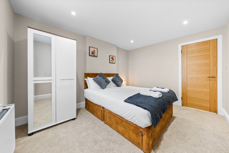Modern bedroom with wooden bed frame, white wardrobe, wooden door and recessed lighting