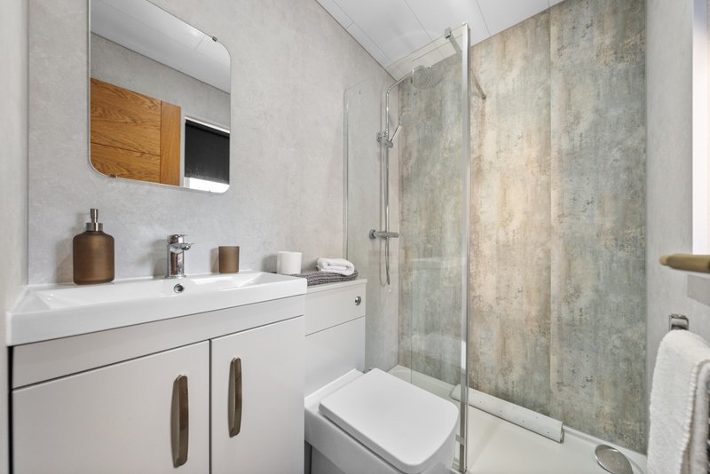 Modern bathroom with white vanity, toilet, walk-in shower with glass screen and stone tiles