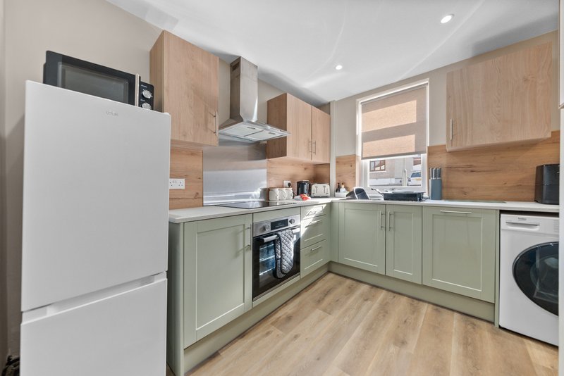 Modern kitchen with sage green cabinetry, wooden upper cupboards, white appliances and wooden flooring