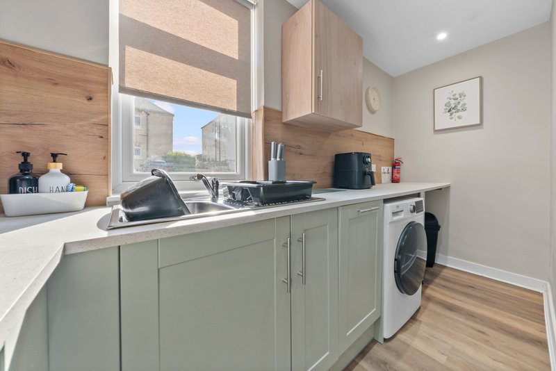 Modern laundry room with green cabinetry, white countertop, washing machine and window overlooking street